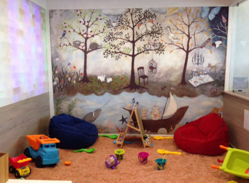 Salinity. Salt room with many kids toys and bean-bag chairs on the ground. The back wall is a mural painted of what appears to be a forrest.