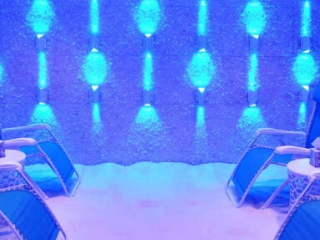The Salt Scene. Salt Room Illuminated By Blue Lights. Lounge Chairs Are Lined Up Against Both Side Walls Facing In.