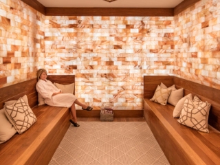 Plam Health. Luxurious Spa Room With Two, Brown Benches Facing Each Other. The Room'S Walls Are Completely Tiled. On The Ceiling, Is A Large, Squared Formation Full Of Salt Rocks. Sitting On One Of The Benches Is A Woman In A White Robe.