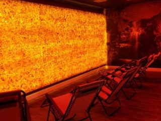 The Salt Cove. Lounge Chairs Lined Up Facing Massive Salt Stone Wall That Is Lit Up Bright Yellow And Orange. Simillar Colors To The Sun.