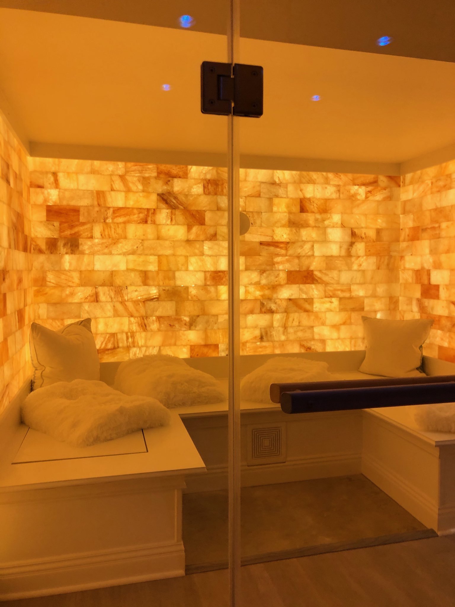 Looking Through Glass At A White Booth With Pillows And An Orange Backlit Salt Stone Wall.