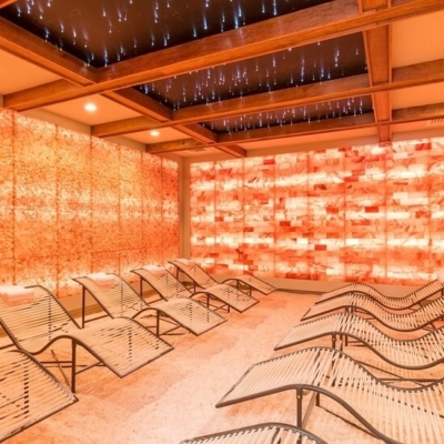 Salt Cave With Nine Chairs On A Salt-Covered Floor With Himalayan Salt Stone Walls And A Back Lit Orange Panel Wall.