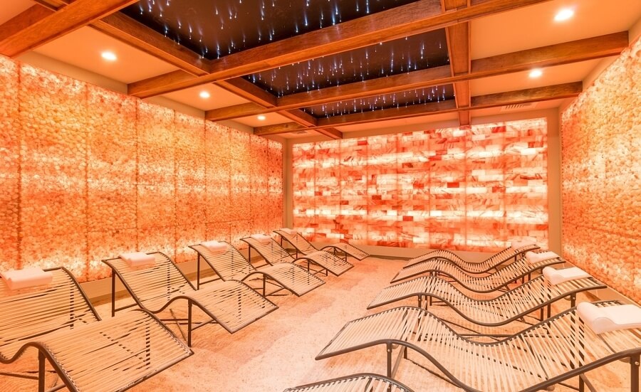 Salt Cave With Nine Chairs On A Salt-Covered Floor With Himalayan Salt Stone Walls And A Back Lit Orange Panel Wall.