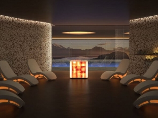 Salt Facility. Large, Luxurious Spa Room With 8 Futuristic Lounge Chairs. A Large Glass Window Reveals A Pool And Mountains In The Background.