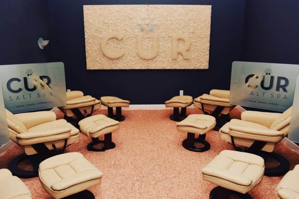 Cur Salt Spa Inc. Large Image mounted on wall spelling out "CUR."  Bright room with 6 cushioned chairs around the room.