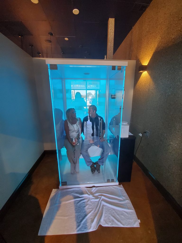 Energy Spa and Tanning. Glass Salt chamber with man and woman inside. Lit by a blue light.