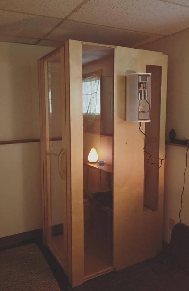 Light wooden and glass salt booth in the corner of the room with a Himalayan salt stone light in the booth.