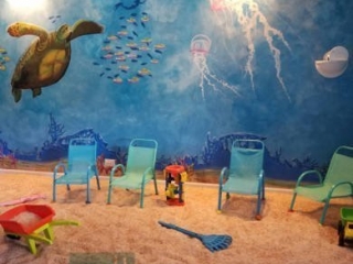 Four small chairs on a salt-covered floor with an ocean painted wall and "Salt north shore salt therapy" on the bottom of the picture.