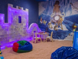 Salt Breeze. Large Salt Room Made For Children. Back Wall Is Painted As An Ice Age Mural And Put Together On The Side Wall Are Salt Blocks In The Shape Of A Castle. On Top Of The Salted Floor Are Bean Bags And Other Toys.