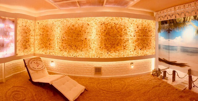 A White Cushioned Chaise On A Himalayan Salt-Covered Floor With Led Lit Salt Walls And Beach Wallpaper.