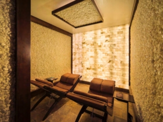 Spa Avania. Two Lounge Chairs Inside Small Salt Room. The Walls Are Covered In Salt Stones And The Front Of The Room Is A Salt Tiled Wall.