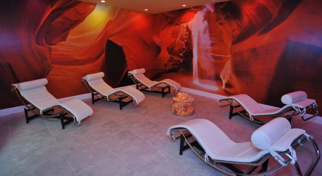 The Salt Station. 5 Lounge Chairs Facing Each Other In Large Spa Room. Walls Are Completely Covered In Pictures Of Red Rock Caves.