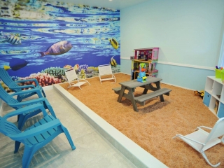 Three blue chairs and a salt-covered children's playpen with three white beach chairs and a picnic table with toys.