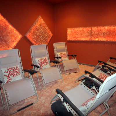 Six Reclining Chairs On A Salt-Covered Floor In A Dark Orange Room With Diamond And Rectangular Himalayan Salt Stone Décor At The Salt Grotto In Valrico, Florida.