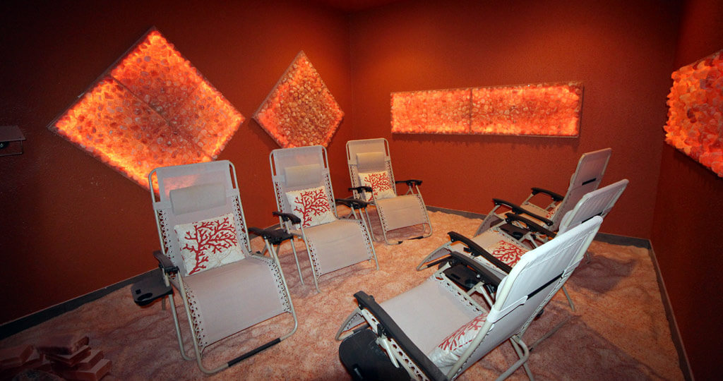Six Reclining Chairs On A Salt-Covered Floor In A Dark Orange Room With Diamond And Rectangular Himalayan Salt Stone Décor At The Salt Grotto In Valrico, Florida.