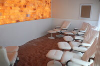 Salt Life Spa. Small Salt room with 6 white chairs and ottomans scattered around the room facing a salt wall.
