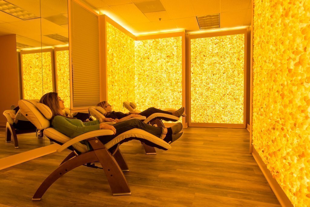 Two women relaxing in reclined chairs in a room surrounded by yellow backlit Himalayan salt stone walls at the Silver Solutions MedSpa in Pittsfield, Massachusetts.