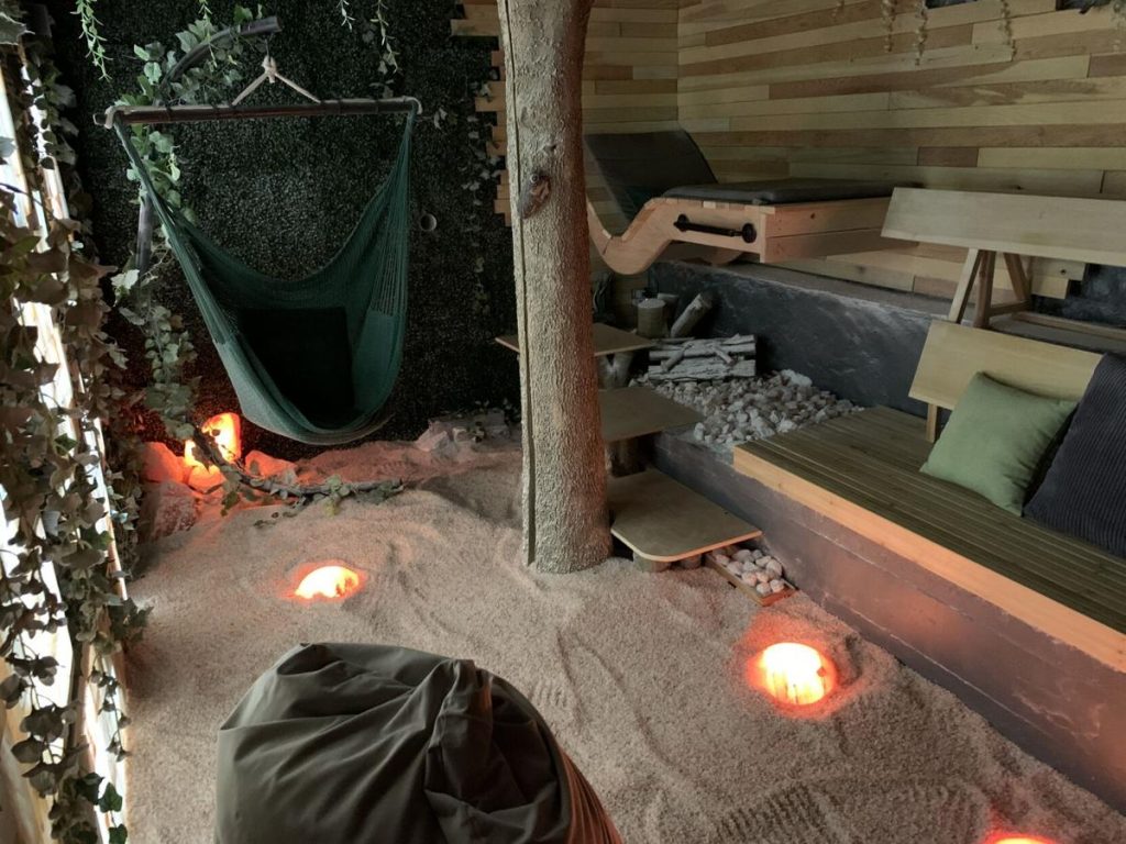 Sukhino Float Center And Salt Cave. Small Salt Room That Has A Jungle Feel To It. The Salt Room Has Multiple Seats And Benches Along With A Hammock, Bean Bag, Glowing Salt Rocks And Vines Wrapped Around The Room