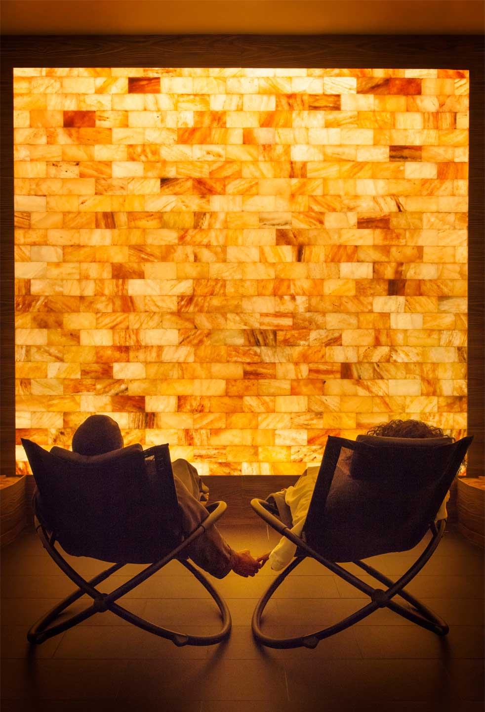 Two people relaxing in lounge chairs in a dimmed room facing a LED backlit salt panel wall at The LINQ Hotel and Casino - Las Vegas, Nevada.