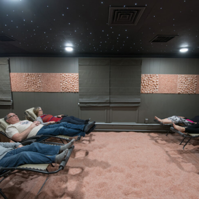 Six Reclining Chairs In A Dark Green Room On A Himalayan Salt-Covered Floor With Three Women And Two Men Relaxing At The Salt Lounge In Wyomissing, Pennsylvania.