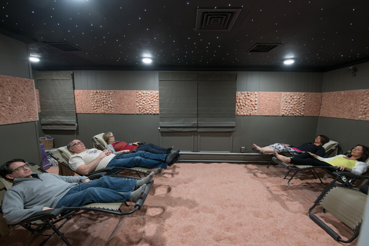 Six Reclining Chairs In A Dark Green Room On A Himalayan Salt-Covered Floor With Three Women And Two Men Relaxing At The Salt Lounge In Wyomissing, Pennsylvania.