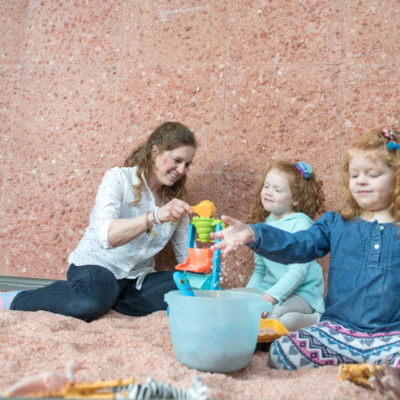 A women and two young girls sitting and playing a salt-covered floor in front of a Himalayan salt stone wall.