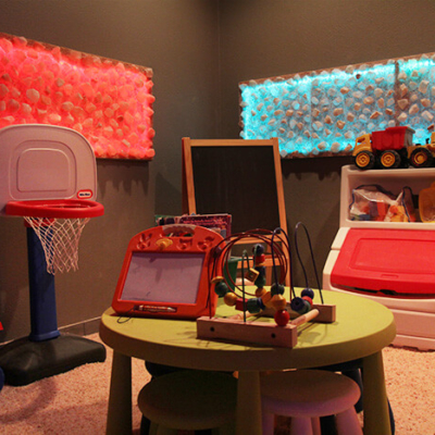Children'S Play Room With Toys, A Mini Basketball Hoop, And A Table On A Salt-Covered Floor With One Red And One Blue Rectangular Backlit Himalayan Salt Décor On The Walls..