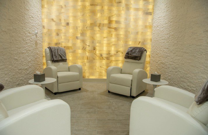 Four white chairs facing each other in a white room with a salt wall backlit by yellow light in Vineyards Country Club in Naples, Florida