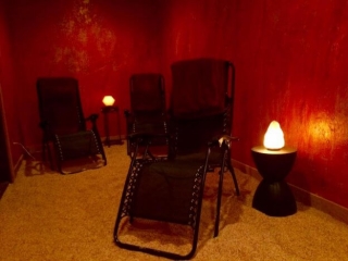 White Orchid Spa. Salt Room With Dark Red Walls And Three Lounge Chairs. Illuminating The Room Are Two Salt Rocks.