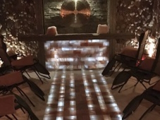 Salt Of The Earth. Dimly Lit Salt Cave With An Illuminated Aisle Runing To The Front Wall. On Either Side Of The Aisle Are Three Chairs.