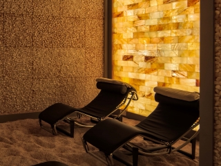 Pura Vida Body And Mind Spa. Two Lounge Chairs In Dimly Lit Salt Room Up Against Tile Wall.