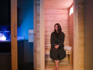 Acadia Spa. At home salt chamber in a dark room with blue light ambiance. A woman in a black robe sits inside of open salt chamber.