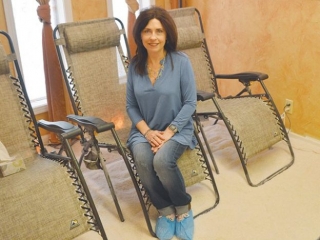 The Salt Retreat At Creative Illusions. Woman Sits Upright In Lounge Chair And Smiles For The Camera.