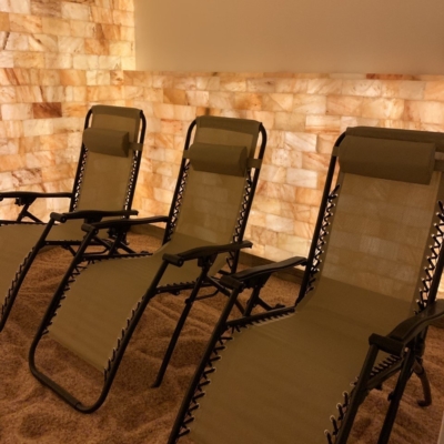 Three reclining chairs in salt room with a salt brick wall behind the chairs backlit by orange lighting at Above and Beyond Yoga Center.