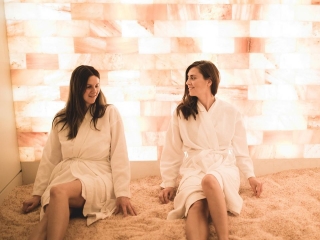 Poppi'S Spa And Lounge. Two Women Sitting On The Salt Floor While Resting Up Against The Tiled Wall Behind Them.