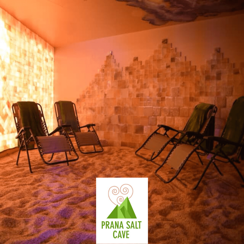 Prana Salt Cave. Four lounge chairs with green towels draped over them, face each other in salt room. Text and logo over picture read: Prana Salt Cave.