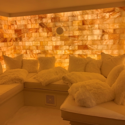White Cushioned Booth With A Variety Of White Pillows And A Salt-Covered Floor With A Backlit Salt Stone Wall At A Private Residence.