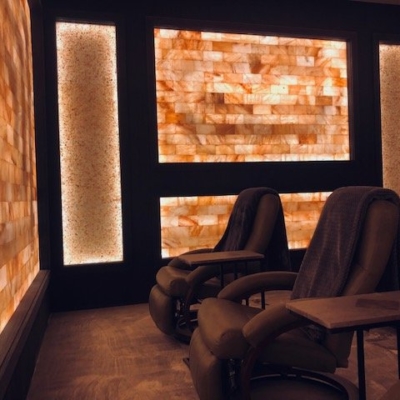 Salt Therapy Room With Salt Stone Panels And Bricks Back Lit With Led Lighting With Three Cushioned Black Chairs.