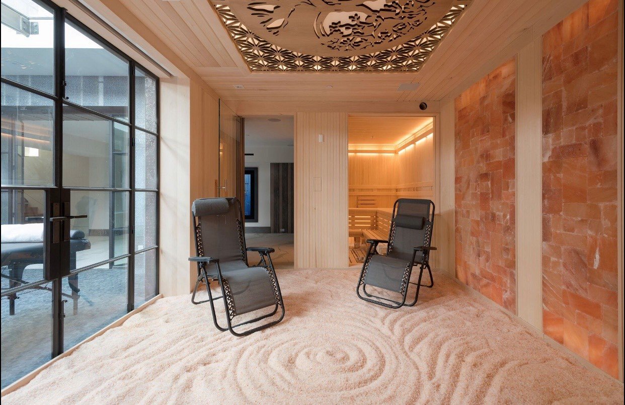 Two grey reclining chairs on a salt-covered floor with a glass door and Himalayan salt stone walls.