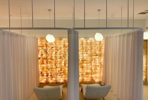 SALT LIVE Energized. Back view of spa room facing empty chairs separated by white curtains in front of salt wall.