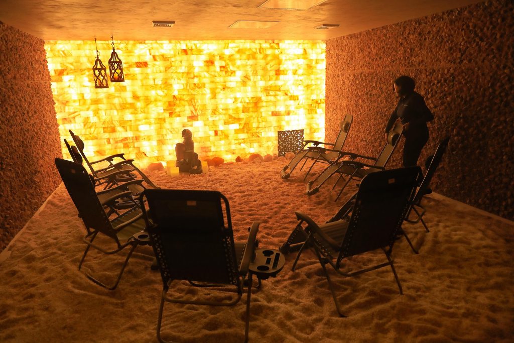 Relax Salt Room. 8 lounge chairs circled up in a salt room. One man appears to be pushing a lounge chair.