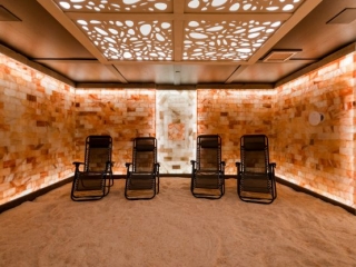 Villa Harrah. Open Spa Room With All Walls Made Up Of Salt Tiles. Four Lounge Chairs Lined Up Next To Each Other On Top Of Salt Covered Floor.