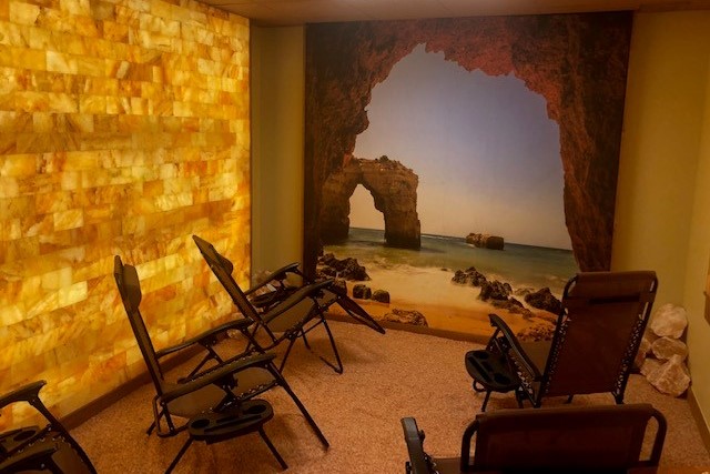 New Genisis Health. 5 lounge chairs inside of salt room while facing a mural of the ocean