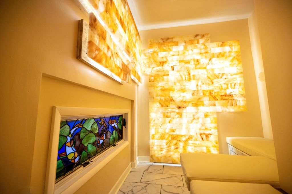 Empowered Healing. Spa room with stained glass, and brightly lit stones on wall.