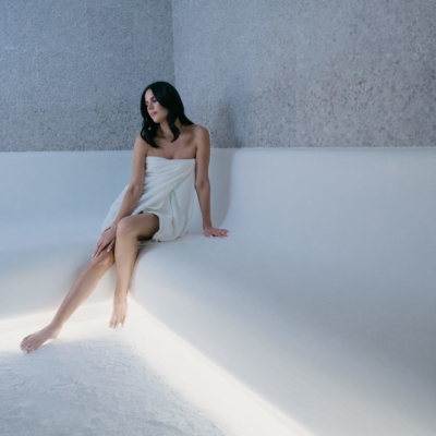 A Brunette Woman In A White Towel Sitting On A White Bench Surrounded By A Grey Salt Panel Wall At The Auberge Beach Residences In Fort Lauderdale, Florida.