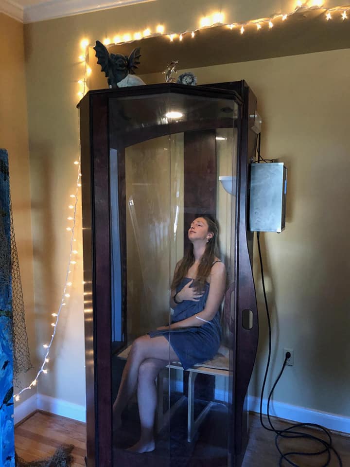 Woman in a towel within a dark wooden and glass salt booth at Infinity More Healing Centre in Catonsville, Maryland
