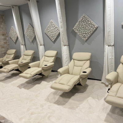 Five white cushioned reclining chairs on a salt-covered floor with a salt stone wall, four white held up separator curtains, and five diamond shaped slat stone decor on the walls.