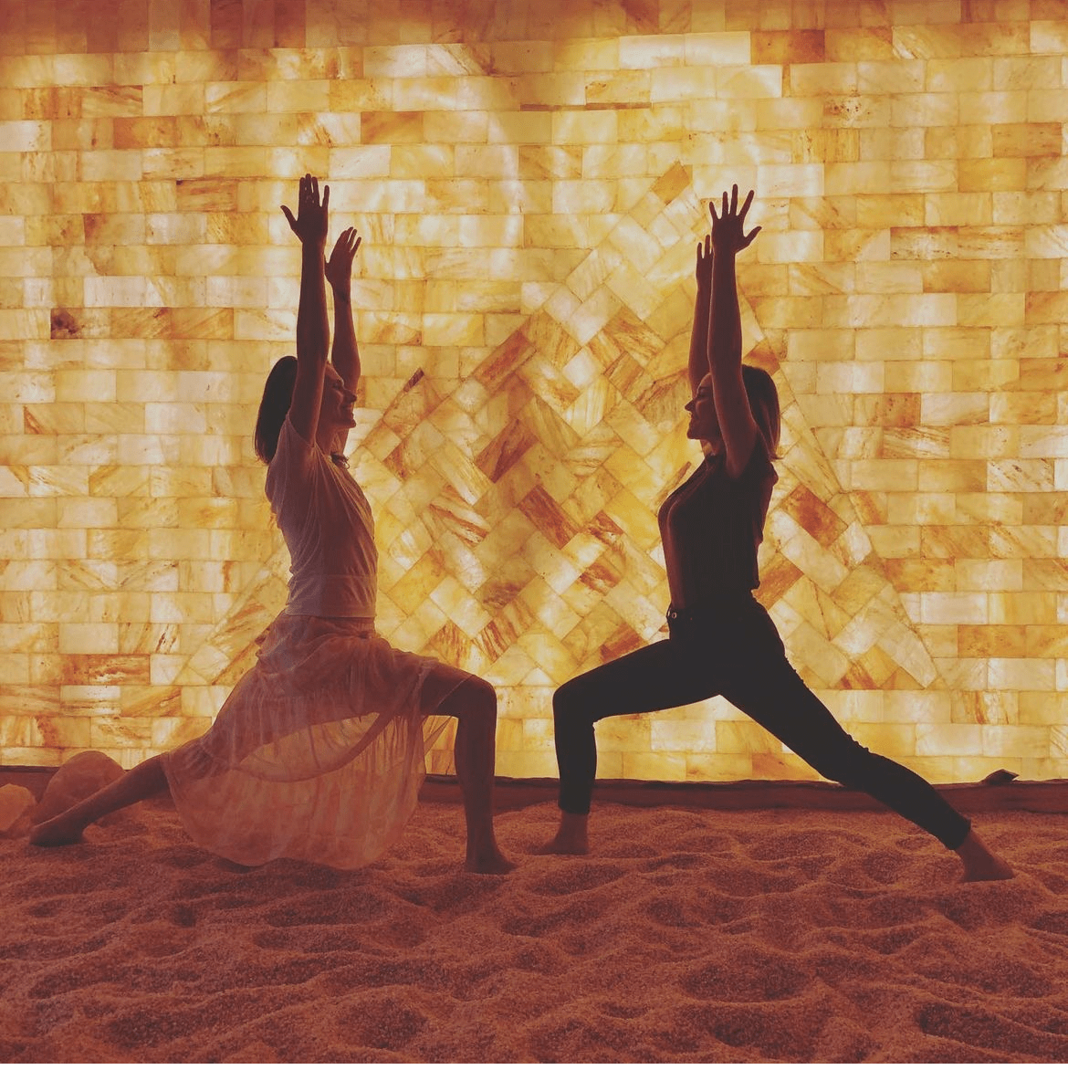 Two women doing yoga in a salt room in front of a Himalayan salt wall with Himalayan salt bricks.