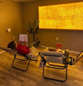 Two People Sitting In Reclining Chairs In The Salt Room At Reset Spa &Amp; Massage Salt Therapy In Saint Marys, Arkansas With Himalayan Salt Panels On The Wall.