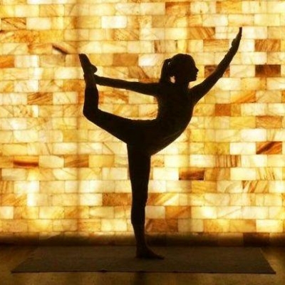 A Woman In A Yoga Pose In A Salt Room In Front Of A Himalayan Salt Brick Wall.